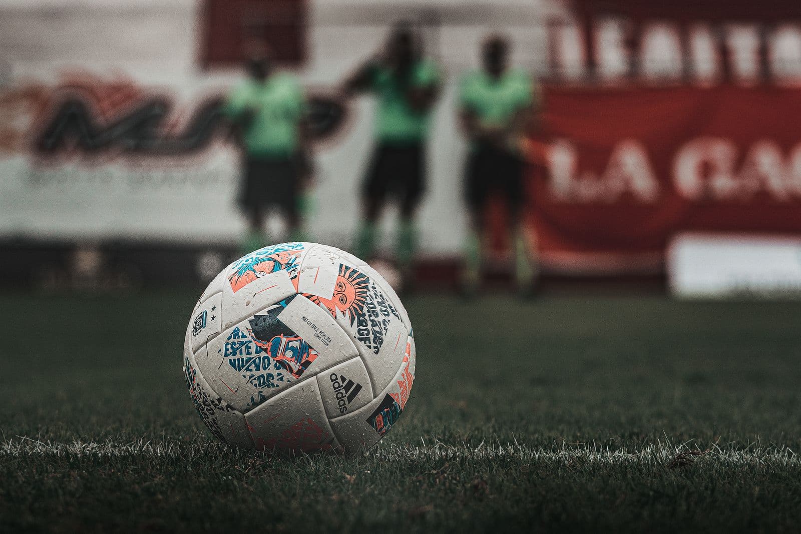 Football resting on grass with players in the background