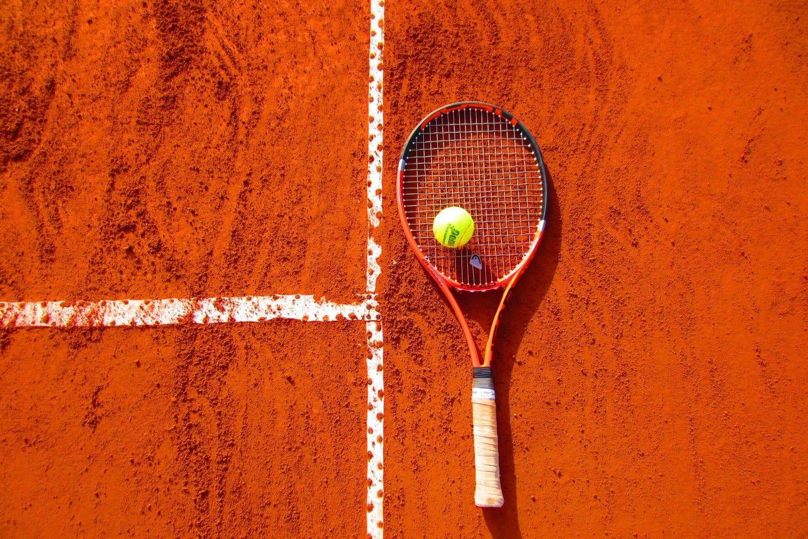 Tennis racket and ball on an orange clay court